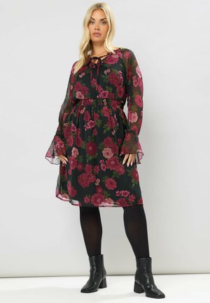 Robe midi florale avec un fond noir, ornée de fleurs bordeaux et vertes, taille élastique, manches longues en tulle et ourlet volanté.