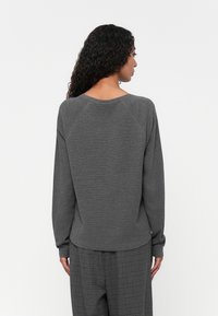 Grå bomullssweatshirt med lange raglanermer, rund halslinje og avslappet passform, sammen med grå rutete bukser.