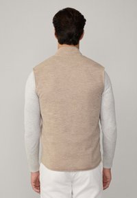Gilet beige senza maniche con una finitura testurizzata, abbinato a una camicia a maniche lunghe grigia chiara. Design semplice, senza hardware o motivi visibili.