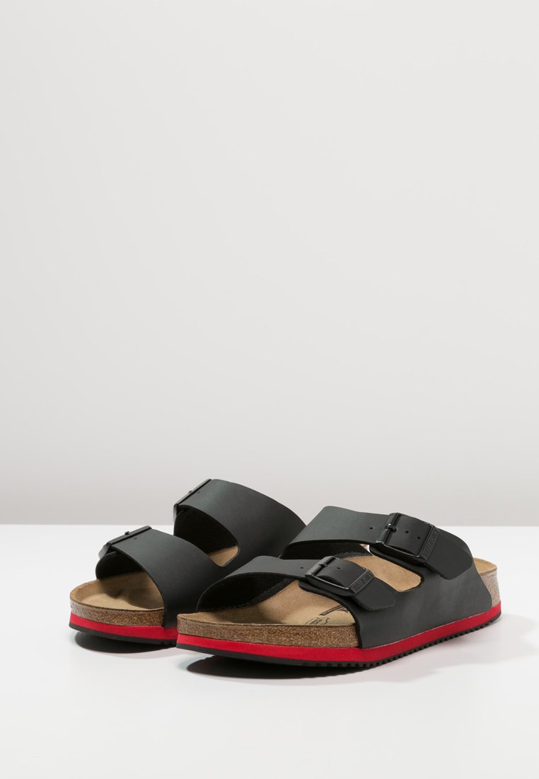 Black sandals with two adjustable straps, cork footbed, and red rubber sole. Smooth texture with metal buckles and lightweight design.