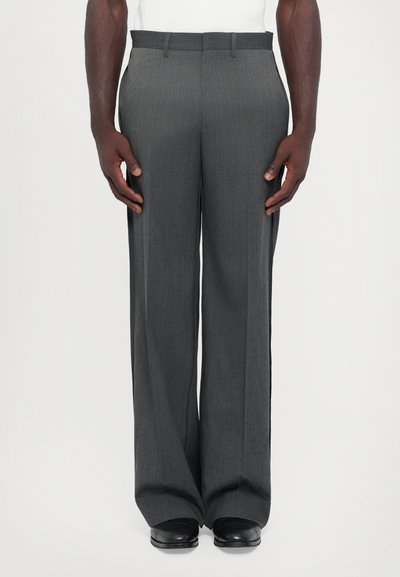 Pantalons de costume gris à la coupe ajustée, présentant un subtil motif vertical, des jambes droites et des passants de ceinture. Association avec des chaussures noires.