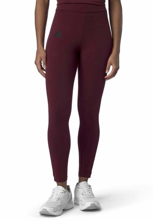 Leggings bordeaux in tessuto elasticizzato con vita alta e piccolo logo nero sull'anca. Abbinati a scarpe da ginnastica bianche.