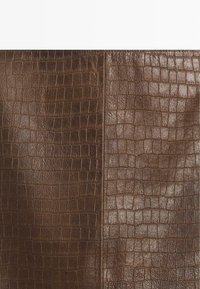 Panneau en cuir marron présentant un motif reptilien texturé avec des écailles surélevées distinctes. La surface est légèrement brillante et lisse.