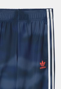 Námořnické modré sportovní šortky s hladkým povrchem, elastickým pasem, bílými bočními pruhy a malým červeným logem Adidas v levém dolním rohu.