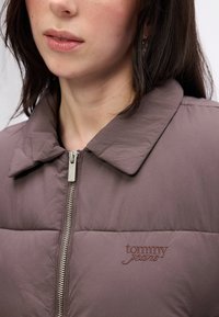 Fioletowa ocieplana kurtka z kołnierzykiem, z przednim zamkiem błyskawicznym i haftowanym logo "tommy jeans" na piersi. Gładka tekstura.