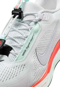 Witte sportschoen met een bovenwerk van mesh, mintgroene accenten, grijs swoosh-logo, zwarte riem en een rood-oranje detail op de tussenzool.