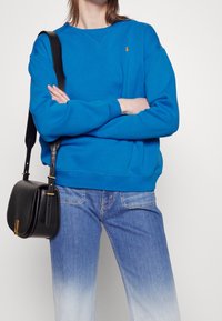 Blå sweatshirt med rund hals, ribbade muddar och nederkant. Matchas med ljusblå jeans. En svart axelväska med gulddetaljer fulländar looken.