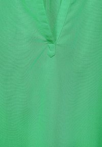 Camicia verde con design a V, realizzata in tessuto morbido. Presenta dettagli di cucitura discreti e una texture leggera.