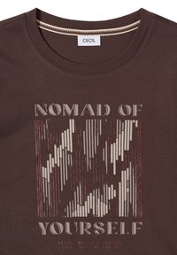 Chemise marron à encolure ronde avec le texte « NOMAD OF YOURSELF » et un motif abstrait de rayures verticales en beige et rouge foncé.