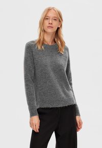 Grå, langærmet sweater lavet af blødt, fluffy materiale med rund udskæring og en let løs pasform, parret med sorte bukser.