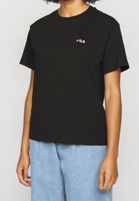 Svart bomullströja med rund hals och korta ärmar. Har en broderad FILA-logotyp i vitt och rött på bröstet. Avslappnad passform.