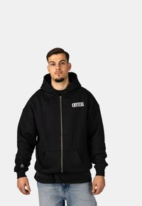 Felpa zip con cappuccio nera realizzata in tessuto misto cotone. Presenta una tasca frontale, polsini a coste e la stampa del logo "CRYSTAL" sul petto.