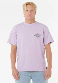 Camiseta de algodón lila con manga corta, cuello redondo, que presenta un diseño de logo en blanco y negro en el lado izquierdo del pecho. Corte relajado.