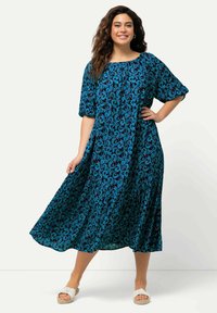 Sininen kukkakuosinen midimekko, jossa on lyhyet puffihihat, pyöreä pääntie ja valuva hame, valmistettu kevyestä kankaasta. Yhdistetty valkoisiin sandaaleihin.