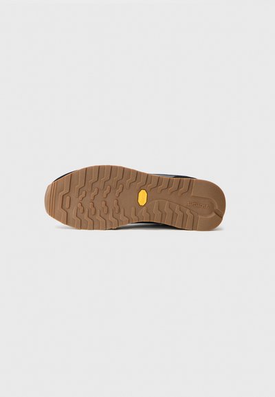 Sole in gomma marrone con un motivo di suola testurizzata, con logo Vibram. La parte superiore della scarpa è nera con un design semplice.