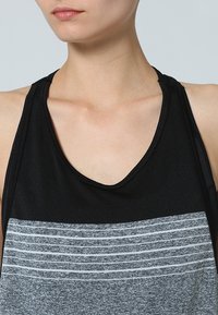 Svart och grå ärmlös sporttop med v-ringning och horisontella ränder på den grå delen, tillverkad i lätt tyg.