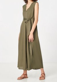 Olivgrön, ärmlös maxiklänning med V-ringning och knytband i midjan. Den har en flödande siluett och mjuk textur.