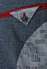 Denim fabric with a blue hue features a patterned gray lining displaying "GENTS CLUB." A red accent and black button detail are visible.
