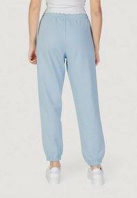 Světle modré tepláky vyrobené z měkké látky, se pružným pasem a manžetami, s volným, uvolněným střihem.