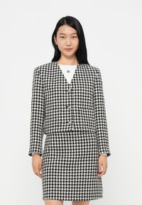 Fekete-fehér houndstooth mintázatú blézer, formázott szabással és passzoló szoknyával, V-nyakkivágással és gombos zárással.
