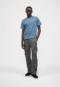 Blå bomull t-skjorte med grafisk logo, kombinert med lys grå cargo-bukser med flere lommer og en avslappet passform. Sorte sko.