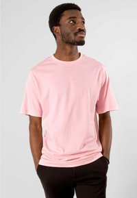 Kort pink bomulds t-shirt med rund hals, korte ærmer og en afslappet pasform, kombineret med sorte bukser. Glat tekstur, ingen synlige mønstre.