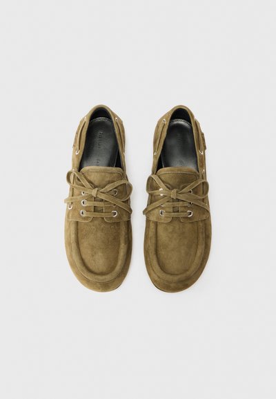Zapatos de ante marrón con puntera redonda, diseño con cordones, ojales plateados y detalles de costura. Plantilla de cuero suave, suelas planas.