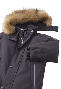 Černá parka s kapucí lemovanou kožešinou, zapínání na zip, patentky a elastické manžety. Má reflexní detaily a postranní kapsy.