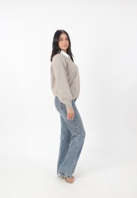 Maglione beige lavorato a maglia con una vestibilità ampia e polsini a costine, abbinato a jeans blu chiaro a zampa d'elefante e sandali con tacco a blocco trasparente.