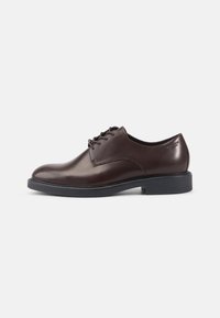 Chaussure habillée en cuir marron avec une finition lisse, un design à lacets, un embout arrondi et une semelle en caoutchouc noire contrastante.
