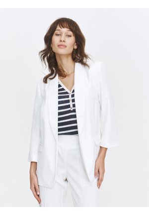 Weißes maßgeschneidertes Blazer mit einem Revers und zwei vorderen Taschen, getragen über einem navy- und weißgestreiften Oberteil. Einfaches Design und leichter Stoff.