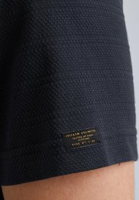 Shorts in tessuto testurizzato blu navy con etichetta tessuta con lettering dorato. La struttura presenta dettagli a costine e un design aderente.