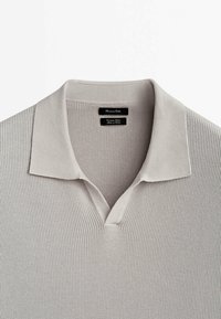 Polo-shirt gris clair avec un motif de tricot texturé, col court et design en V. Comprend deux étiquettes de marque à l'intérieur.