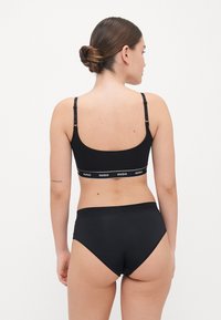 Completo bikini sportivo nero composto da un reggiseno a fascia con schiena racerback, spalline regolabili e banda con logo, abbinato a un slip a vita alta. Texture liscia.