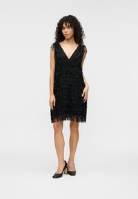 Μαύρο φόρεμα με κρόσσια, V-λαιμόκοψη και κοντά μανίκια πεταλούδας. Κατασκευασμένο από υφασμάτινη υφή, φτάνει πάνω από το γόνατο και διαθέτει χαλαρή σιλουέτα.