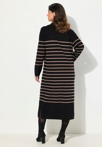 Robe noire longue avec des rayures beige horizontales, décolleté rond et fentes latérales. Fabriquée en tissu doux, elle présente des manches longues et une coupe décontractée.
