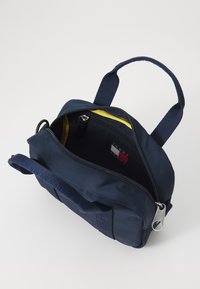 Sac navy avec un intérieur jaune, fermeture éclair, doubles poignées et une étiquette de logo à l'intérieur. Fabriqué en matériau durable avec une texture lisse.