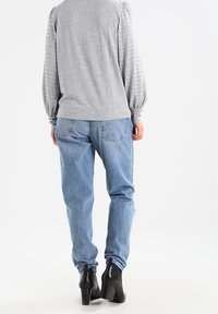 Light grey long-sleeve top with ribbed pattern and puff sleeves paired with light blue straight-leg jeans and black heeled ankle boots.