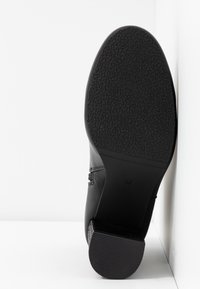 Chaussure noire en cuir avec une semelle en caoutchouc texturée. Présente un talon bas et une finition lisse. Taille indiquée comme 37 à l'intérieur.