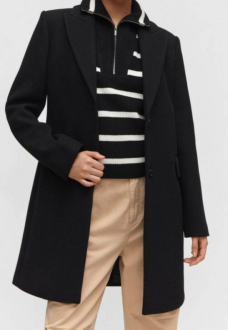 Schwarzer Wollmantel mit Reverskragen, Ein-Knopf-Verschluss und Seitentaschen, getragen über einem schwarz-weißen gestreiften Pullover und beigen Hosen.