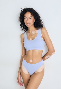 Ensemble de bikini à coprs côtelés bleu clair, comprenant un haut à col en scoop et un bas taille haute, fabriqué en tissu lisse et extensible. Variations de teintes de peau visibles.