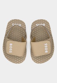 Ζευγάρι μπεζ σανδαλιών με σχέδια και ρυθμιζόμενους ιμάντες που φέρουν την ένδειξη "BOSS" σε μπεζ υφασμένους πάτους.