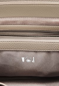 Interno di una borsa beige testurizzata con più scomparti, cerniere argentate e un motivo di icone relative al maquillaje su uno sfondo in tessuto liscio.