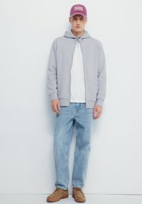 Szara bluza z kapturem zapinana na zamek na biały t-shirta, jasnoniebieskie dżinsy i brązowe buty; zestawione z fioletową czapką z haftem "PARIS".