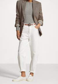 Personne portant un blazer en chevrons marron, un pull gris à torsades, un pantalon blanc taille haute avec une ceinture marron, et des baskets blanches.