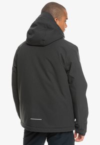 Schwarze Kapuzenjacke mit glatter Textur und lockerer Passform. Hat einen weißen Akzent am Saum und eine große Kapuze. Rückansicht gezeigt.