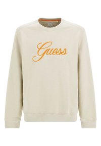 Sweatshirt beige en tissu doux, avec manches longues et col rond. Logo "Guess" brodé en orange avec l'année de création.