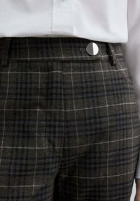 Pantalons à carreaux gris avec un motif à checker et des accents bleus et blancs. La taille présente un fermoir en métal rond et une texture lisse.