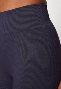 Tamsūs juostuoti aukšto liemens leggingai, rodančiais tekstūruotą audinį su minkštu paviršiumi. Liemens juosta yra stora ir elastinga, kad suteiktų papildomą palaikymą.