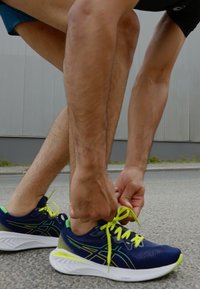 Scarpe da corsa blu con lacci e dettagli gialli. Parte superiore in tessuto texture, suola imbottita, logo visibile sul lato e dettagli riflettenti.